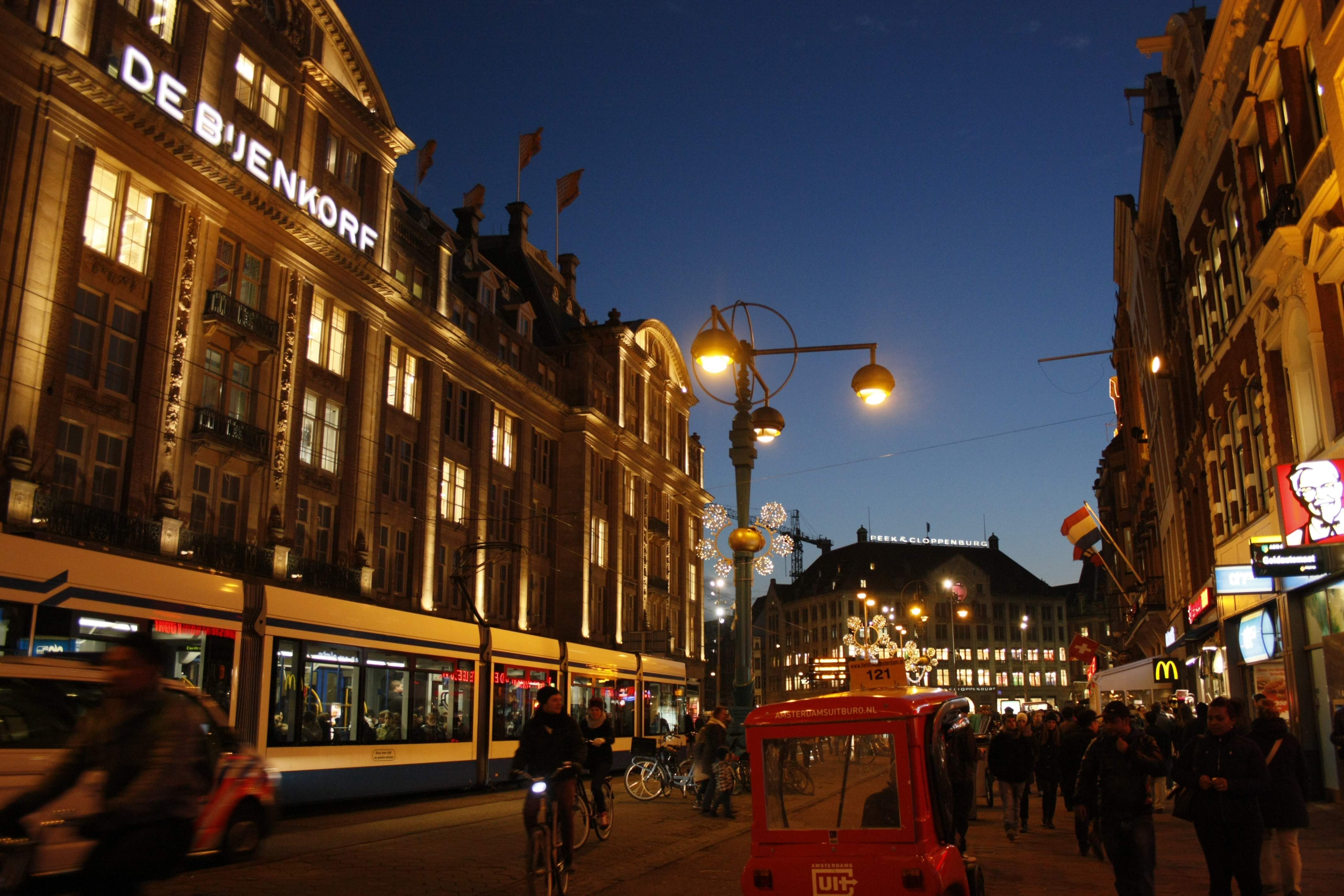 An urban space after sunset packed with people and public transport and lighting on buildings